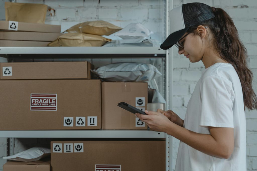 Mujer gestionando almacén con cajas al fondo.